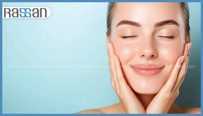 Syn Ake یا بوتاکس؟ کدام یک برای جوانسازی پوست بهتر است؟ 4 زنی جوان با چشمهای بسته و لبخند ملایم که دستهایش را روی گونههای مرطوب، براق و بدون چروک خود گذاشته است.