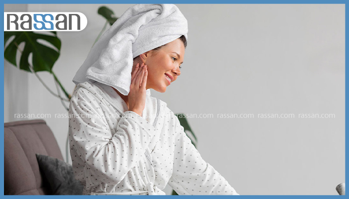 زن محجبه در فضای روشن خانه در حال ماساژ دادن آبرسان سبک و فاقد چربی روی پوست صورت