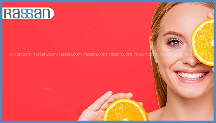 ژل ویتامین C را صبح بزنیم یا شب؟ 2 زنی جوان با لبخند درخشان که یک برش پرتقال را جلوی چشمش گرفته و برش دیگری در دست دارد با پسزمینه قرمز