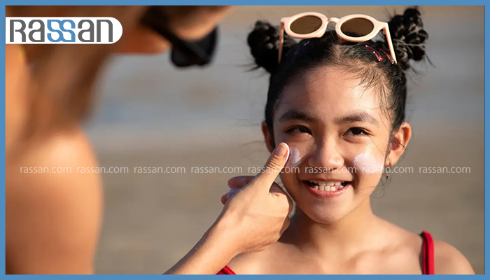 از چه سنی ضد آفتاب برای کودک ضروری است؟ 2 زدن ضد آفتاب روی گونههای دختر بچه لبخند به لب در ساحل دریا