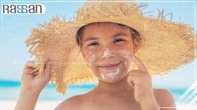 دختر بچه با کلاه حصیری و کرم ضد آفتاب روی صورت در محیط ساحلی