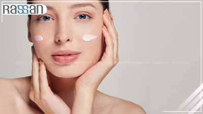 زنی در حال مالیدن کرم ضد آفتاب روی گونه خود در فضای باز و زیر نور خورشید برای پیشگیری از لک صورت